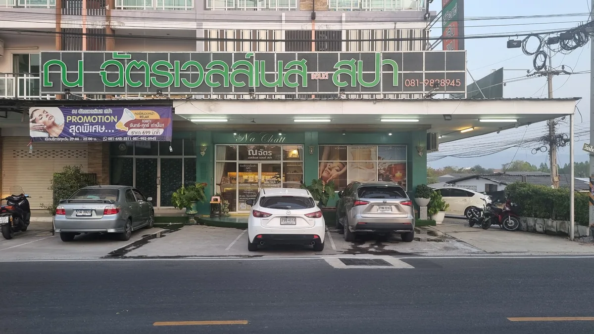 ด้านหน้าร้านณฉัตร เวลเนส แอนด์ สปา มองจากถนนใหญ่ เห็นป้ายชื่อร้านและรถที่จอดอยู่
