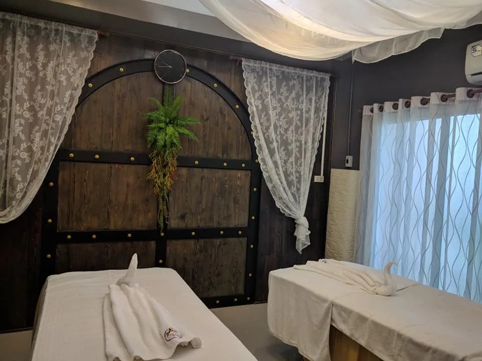 ห้องทรีตเมนต์สองเตียงที่มีผ้าม่านผ้าขาวผูกไว้และโคมไฟติดผนัง
